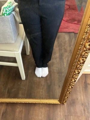 Svarta kostymbyxor med rak passform - Säljer ett par klassiska svarta kostymbyxor med rak passform och hög midja. Byxorna har pressveck framtill och stängs med dragkedja och knapp. Perfekta till en snygg och stilren look.