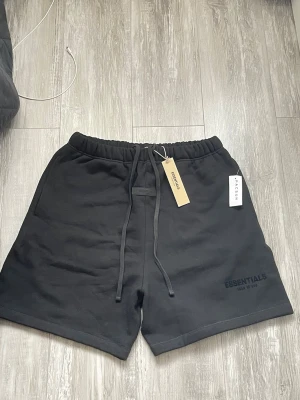  Essentials Fear of God Sweat Shorts – Helt Nya (Tags kvar) - Säljer nu ett par helt oanvända Essentials shorts (Fear of God) i färgen svart. Detta är den klassiska sweatshirt-modellen i tjockt och skönt material, perfekta för sommaren eller hemmahäng 