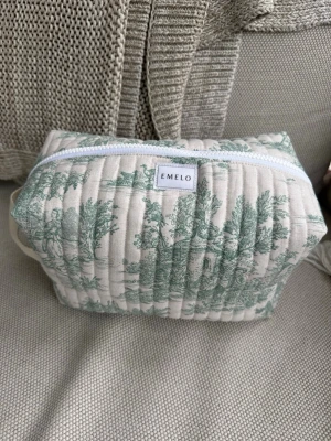 Quiltad necessär från Emelo - Säljer en quiltad necessär från Emelo i beige bomullstyg med grönt vintageinspirerat mönster. Väskan har dragkedja upptill och en praktisk handrem på sidan. Perfekt för smink eller småprylar när du är på språng. Beige insida med innerfack. Mått ca 27x17x12 cm