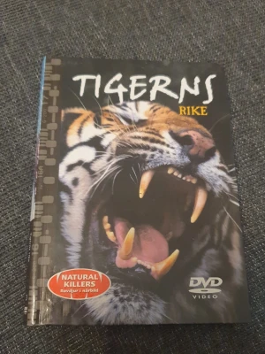 Tigerns rike DVD-bok - En bok med tillhörande DVD från serien Natural Killers, med titeln 'Tigerns rike'. Omslaget har en närbild på en rytande tiger och boken ger en fascinerande inblick i tigerfamiljens liv. Perfekt för dig som gillar djur och naturdokumentärer.