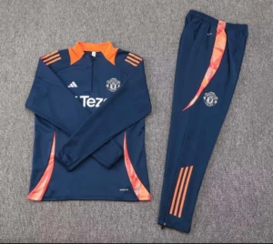 Manchester United träningsset blå/orange - Snyggt träningsset från Adidas för Manchester United med långärmad tröja och matchande byxor i mörkblått. Setet har orange detaljer, klubbmärke på både tröja och byxa samt dragkedja vid halsen. Perfekt för fotbollsträning eller chill.