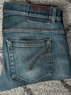 dondup george - Säljer ett par blå skinny jeans från dondup med slitningar och rivna detaljer på benen. Jeansen har klassisk femficksdesign, snygga kontrastsömmar och en cool tvättad look. Perfekta för dig som gillar en trendig och avslappnad stil.