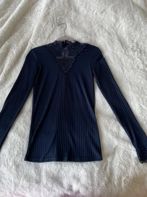 Mörkblå ribbad blus med spetsdetalj - Supersnygg mörkblå långärmad topp med ribbad struktur och detaljerad spets vid halsen. Toppen har en v-ringad spetskant.