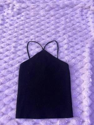 Svart ribbad linnetopp - Snygg svart ribbad linnetopp med tunna axelband och rak passform. Perfekt att styla med jeans eller kjol för en trendig look. Materialet är mjukt och stretchigt för extra komfort.