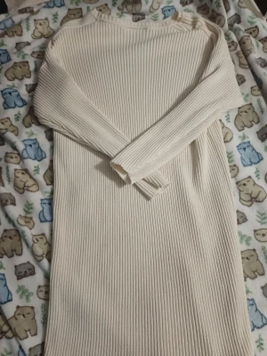 Ribbad beige långärmad klänning - Snygg ribbad klänning i beige med lång ärm och rund hals. Klänningen är stickad och har en rak, enkel passform som passar perfekt till många olika stilar. Perfekt för dig som gillar en stilren och mysig look.