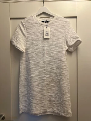 Vit kort klänning från BikBok - En stilren vit kort klänning från Zara i strukturerat tyg. Klänningen har rund halsringning och korta ärmar, med en rak och enkel passform som ger en clean look. Perfekt för dig som gillar minimalistisk stil.