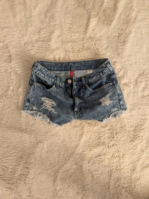 Blå jeansshorts från H&M Divided - Snygga blå jeansshorts från H&M Divided med råa kanter och klassiska bakfickor. Perfekta för varma dagar och har en avslappnad vibe. Gjorda i bomull för en skön känsla. 