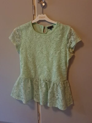 Mintgrön spetsblus med volang - Superfin mintgrön blus från Kappahl 2000s vintage med korta ärmar och volang nertill. Blusen är täckt av spets med blommigt mönster och har en söt knappdetalj i nacken. Perfekt för dig som gillar romantisk och feministisk stil. Storlek 164 känns som XS