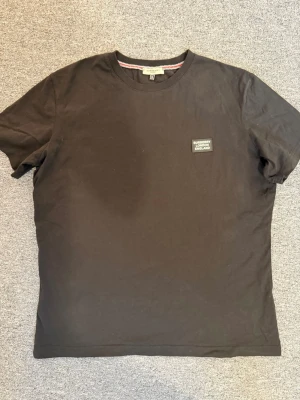 Svart Burberry t-shirt med logga - Svart t-shirt från Burberry med klassisk rund hals och en snygg patch med 'Burberry London England' på bröstet. Hör av dig vid funderingar och behov av fler bilder