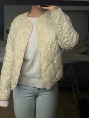 Mango jacka  - Säljer en krämvit pufferjacka med rund halsringning och tryckknappar framtill. Jackan har ett quiltat mönster och är lätt vadderad. Modellen är boxy och kortare i passformen.