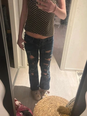Mörkblå slitna bootcut jeans - Säljer ett par mörkblå bootcut jeans med rejält slitna detaljer och hål framtill på båda benen. Jeansen har klassisk femficksmodell och låg midja. Perfekta för en edgy och avslappnad stil. Har sytt de low waist men det är inget som märks. Midjemått ca 41cm rakt över och innerbenslängd ca 75cm. 