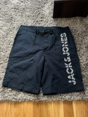 Marinblå badbyxor Jack & Jones - Snygga marinblå badbyxor från Jack & Jones med vit logga längs benet. snabbtorkande material. Perfekta för stranden eller poolen. Helt ny aldrig använd 