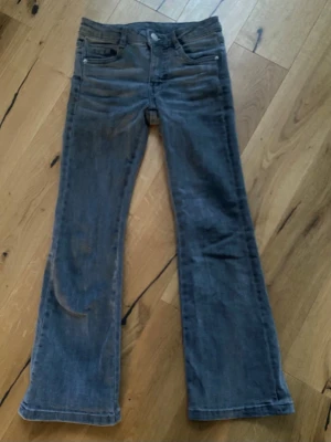 Grå bootcut jeans från Kappahl - Snygga grå bootcut jeans från Kappahl med klassisk femficksdesign och knappgylf. Jeansen har en lätt utsvängd passform nertill och justerbar midja på insidan. Perfekta för en avslappnad och trendig look.