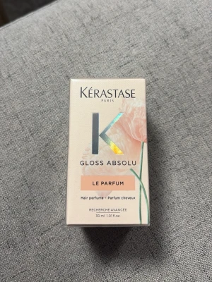 Kérastase Gloss Absolu Le Parfum - Kérastase Gloss Absolu Le Parfum är en hårparfym i en stilren ljusrosa kartong med holografiska detaljer och blommotiv. Förpackningen innehåller 30 ml och ger håret en fräsch och lyxig doft.