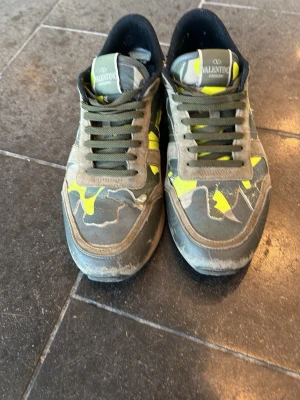 Valentino rockrunner  - Snygga sneakers från Valentino med grått och grönt camomönster samt detaljer i neon-gult. Skorna har låga skaft, gröna skosnören och en robust sula. Märkeslogga på plösen och insidan. Perfekta för dig som vill sticka ut med en unik och trendig look. Pris kan diskuteras vid smidig affär