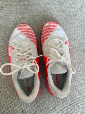 Vita och röda Nike träningsskor - Snygga träningsskor från Nike i vitt med röda detaljer och logga. Ovandelen är i meshmaterial för bra ventilation och skon har en unik sula med röd förstärkning på sidan. Perfekta för gym eller inomhusträning. Använda 2 gånger!