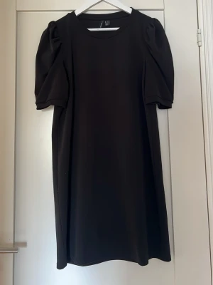 Svart klänning med puffärm Vero Moda - Svart klänning från Vero Moda med rund halsringning och trendiga puffärmar. Modellen är rak och har en enkel, stilren design som passar perfekt till många tillfällen. Tillverkad i ett mjukt material som känns bekvämt mot huden.