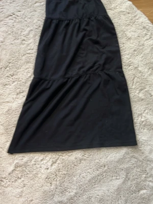 Svart långklänning från Kappahl - En svart långklänning från Kappahl med volangdetaljer i flera lager. Klänningen har en enkel och stilren design, perfekt för dig som gillar klassiska plagg. Tillverkad i ett mjukt och följsamt material.