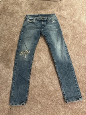 Blå slitna Diesel jeans med hål - Säljer ett par blå jeans med slim fit och slitningar, inklusive ett stort hål på vänster lår. Jeansen har klassisk femficksdesign och ljus tvätt. Perfekta för en avslappnad och trendig stil. Jeansen har längden 34 och är 31 i midjan används 3-4 gånger . Köpte för 2400 