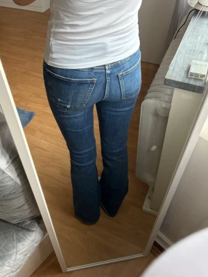 Blå bootcut jeans  - Säljer ett par klassiska blå bootcut jeans med låg/normalhög midja och fem fickor. Jeansen har en snygg tvätt och subtila slitningar för en avslappnad look. Säljer då de blivit för små
