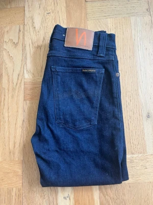 Nudie Jeans - Snygga mörkblå skinny jeans från Nudie Jeans med klassisk femficksdesign och läderpatch med logga bak. Jeansen har en smal passform och är tillverkade i stretchigt denimtyg för extra komfort. Perfekta för en stilren och modern look. Modell: High Kai slim fit w28 l34