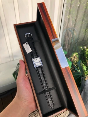 Snygg och elegant läderklocka från cosmos Sweden  - Stilren NY med etikett klocka från cosmos med fyrkantig silverfärgad boett och svart läderarmband med struktur. Urtavlan är vit med romerska siffror och blå visare. Perfekt accessoar för dig som gillar klassisk och tidlös design. Snabb leverans 