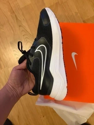 Svarta Nike sneakers med vit sula - Snygga svarta sneakers från Nike med vit sula och klassisk vit swoosh på sidan. Ovandelen är i mesh för bra andningsförmåga och skon har svarta snören. Perfekta för en sportig och stilren look.