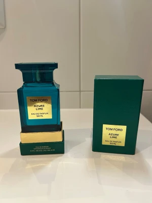 Tom Ford Azure Lime Eau de Parfum - Tom Ford Azure Lime Eau de Parfum 100 ml i en lyxig blågrön glasflaska med gulddetaljer. Parfymen levereras i en matchande grön ask med guldfärgad etikett. Flaskan har en elegant, fyrkantig form och exklusiv känsla.