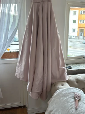 Ljuslila långklänning med snörning - Elegant långklänning i ljuslila nyans med vacker snörning i ryggen och markerad midja. Klänningen har en vid, svepande kjol och är axelbandslös, perfekt för speciella tillfällen. Materialet känns slätt och har ett fint fall.