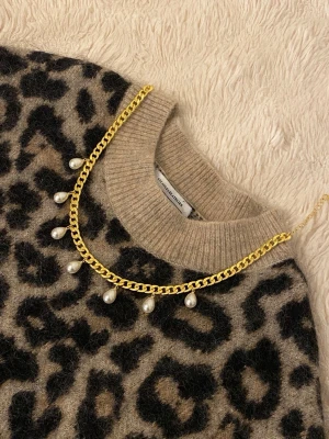 Guldhalsband med droppformade pärlor - Snyggt halsband i guldfärgad metall med sex droppformade vita pärlor som hänger längs kedjan. Kedjan har en chunky design och pärlorna ger en elegant touch. Perfekt för att lyfta vilken outfit som helst.