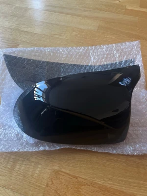 Svart backspegelkåpa till bil - Säljer en svart backspegelkåpa till bil, tillverkad i blank plast. Kåpan har en modern och aerodynamisk form och passar perfekt som ersättningsdel. Perfekt för dig som vill fräscha upp bilens utseende.