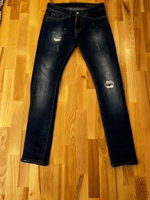 Mörkblå Dsquared2 jeans - Snygga mörkblå jeans från Dsquared2 med slitna detaljer och klassisk femficksmodell. Jeansen har kontrastsömmar och en läderpatch med logga bak i midjan. Perfekta för dig som gillar streetwear och vill ha en trendig look.