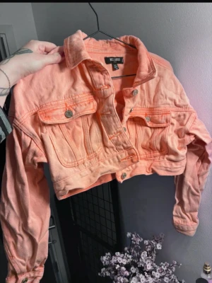 Korta jeansjacka i peach från Missguided - Snygg croppad jeansjacka i peach/ljusorange från Wild Child. Klassisk modell med två bröstfickor med knappar och krage. Jackan har långa ärmar och coola detaljer i sömmarna. Perfekt för att lyfta din outfit med färg.