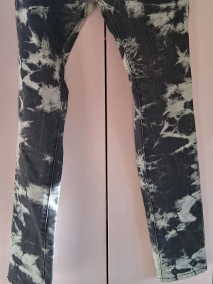 Svarta tie dye jeans med raka ben - Unika svarta jeans med vit tie dye-effekt och raka ben. Snyggt mönster som sticker ut och ger en cool vibe. Klassisk femficksmodell i denim, perfekt för dig som vill ha något annorlunda i garderoben. Aldrig använda då dom va för små för mig