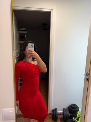 Röd oneshoulder klänning - Snygg röd oneshoulder klänning med lång ärm på ena sidan och slits nertill. Tight passform som framhäver figuren och stretchigt material. 