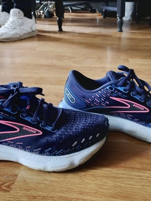 Brooks Glycerin blå sneakers Strlk 40.5 - Snygga Brooks Glycerin sneakers i marinblått med detaljer i rosa och ljusblått. Ovandelen är i mesh för bra andningsförmåga och sulan är tjock och vit för extra komfort. Perfekta för dig som gillar sportig stil och vill ha riktigt sköna skor. Dom är i nyskick och använda ett fåtal gånger.