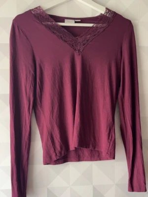 Vinröd långärmad topp med spets - Vinröd långärmad topp från Gina Tricot med v-ringning och dekorativ spets runt halsen. Toppens material känns mjukt och stretchigt, perfekt för en snygg och bekväm look. Passar dig som gillar stilrena detaljer och en feminin touch.