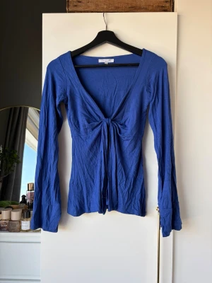 Blå långärmad topp med knyt - Snygg blå långärmad topp med v-ringning och knyt framtill. Tunn och mjuk i bomull, perfekt att styla med jeans eller kjol. Toppen har en figurnära passform och långa ärmar.