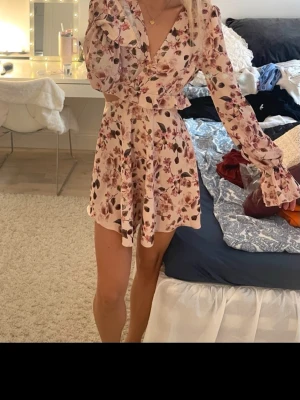 Blommig omlottklänning i ljusa toner - Söt kort omlottklänning med blommigt mönster. Klänningen har en supersnygg cut out som framhäver midjan❤️ Perfekt för sommarens alla tillfällen❤️