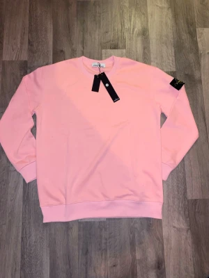 Rosa sweatshirt från Stone Island - Snygg rosa sweatshirt från Stone Island med klassisk rund hals och ribbade muddar. Tröjan har en stilren design och ikonisk logga på ärmen. Perfekt för en avslappnad och trendig look.