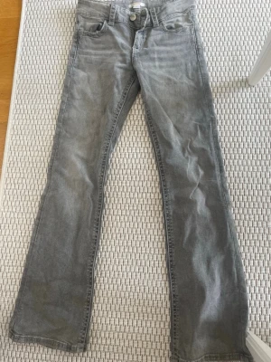 Grå bootcut jeans med broderade fickor - Snygga grå jeans med bootcut-modell och coola broderade detaljer på bakfickorna. Klassisk femficksdesign och knappgylf. Perfekta för dig som vill ha en avslappnad men ändå unik stil.