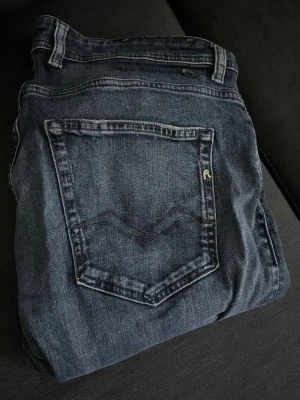 Mörkblå replay grover jeans - Mörkblå jeans från Replay med klassisk femficksdesign och diskreta slitningar. Jeansen har raka ben och tydliga sömmar på bakfickorna. Waist 32 och length 34.