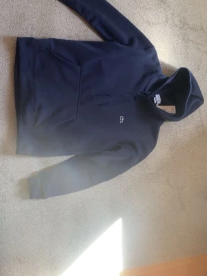 Mörkblå hoodie från Lacoste - Snygg mörkblå hoodie från Lacoste med klassisk krokodillogga på bröstet. Hoodien har huva med dragsko och en stor magficka framtill. 