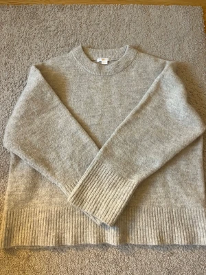 Beige stickad tröja Gina Tricot - Mysig beige stickad tröja från Gina Tricot med rund halsringning och breda ribbade muddar vid ärmslut och nederkant. Tröjan har en enkel och stilren design som passar perfekt till höst och vinter. Materialet känns mjukt och skönt mot huden.