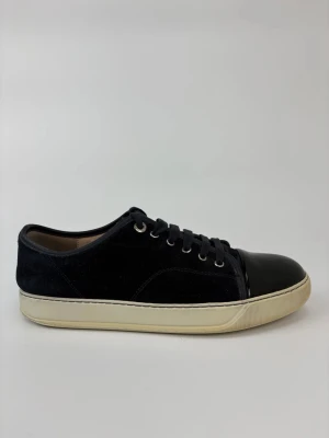 Svarta Lanvin sneakers med lackad tå - Stilrena svarta sneakers med ovandel i mocka och en glansig, lackad tå. Skorna har vita sulor och svarta skosnören. Perfekta för dig som vill ha en clean look med en twist. Metallfärgade öljetter ger extra detalj.