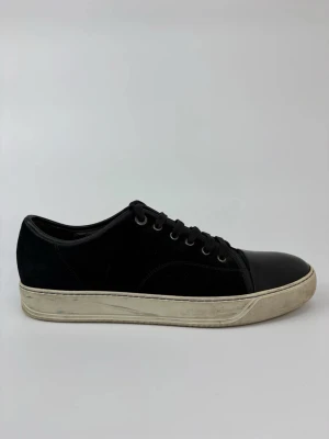 Svarta Lanvin låga sneakers med gummitå - Stilrena svarta sneakers med lågt skaft, svart mocka och läderdetaljer på tån. Skorna har svarta snören och en vit, något smutsad gummisula som ger en cool kontrast. Perfekta för en avslappnad streetstil.