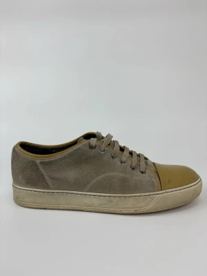 Beige Lanvin sneakers med mocka och lackad tå - Sneakers i beige mocka med snörning och en glansig, lackad tå i ljusbrun färg. Snygg kontrast mellan material och färg, perfekt för dig som gillar stilrena men unika detaljer. Klassisk låg modell med gummisula.