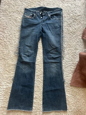 Blå bootcut jeans från Diesel - Säljer ett par blå bootcut jeans från Diesel med råa kanter och slitna detaljer. Jeansen är låg midjade . Köpt från Sellpy med slits men har själv sytt ihop dem. Riktigt coola och unik💕🤗