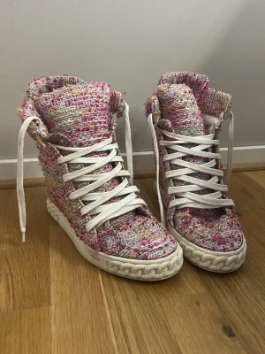 Färgglada tweed high top sneakers - Unika high top sneakers i tweedtyg med rosa, vita, gula och lila toner. Skorna har vita snören och en vit sula med diskret mönster. Perfekt för dig som vill sticka ut med en färgglad och trendig look. Materialet är textil med en grov struktur. Aldrig använda av mig, men köpta av en annan kreatör här på Vinted.