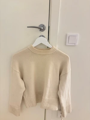 Beige stickad tröja med ribbade detaljer - Snygg beige stickad tröja med ribbade muddar vid ärmslut, nederkant och halsringning. Tröjan har en rak passform med lång ärm. Enkel att matcha med olika outfits. Den perfekta stickade tröjan! Så stilren.
